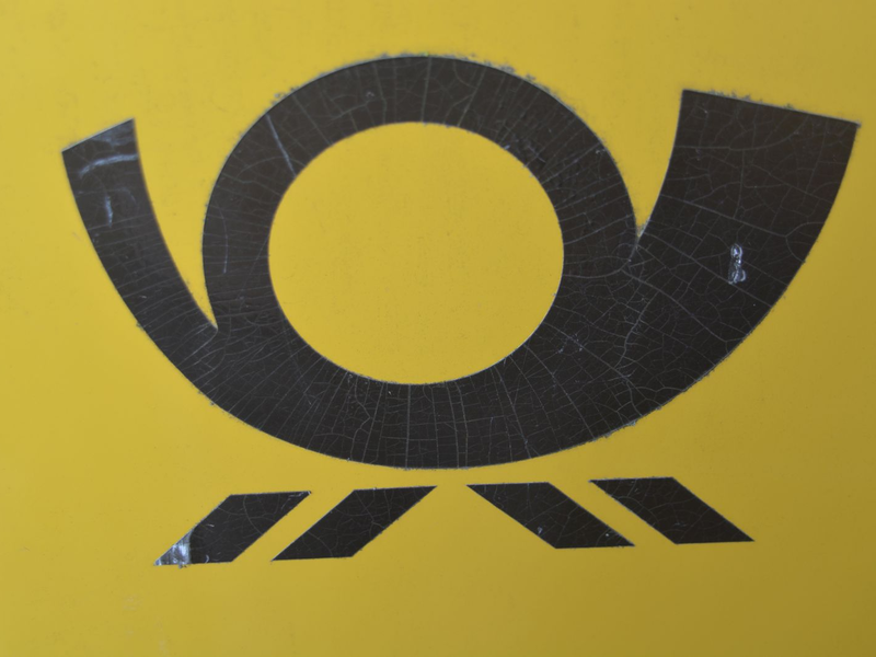Auf einem gelben Briefkasten klebt das schwarze Posthorn.