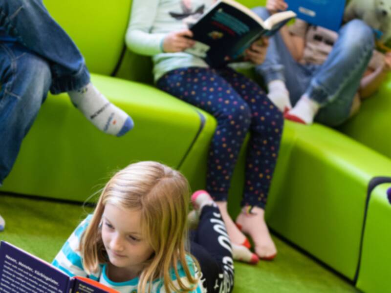 Kinder stzen auf einer grünen Couch und auf dem Teppich und lesen Bücher und Zeitschriften