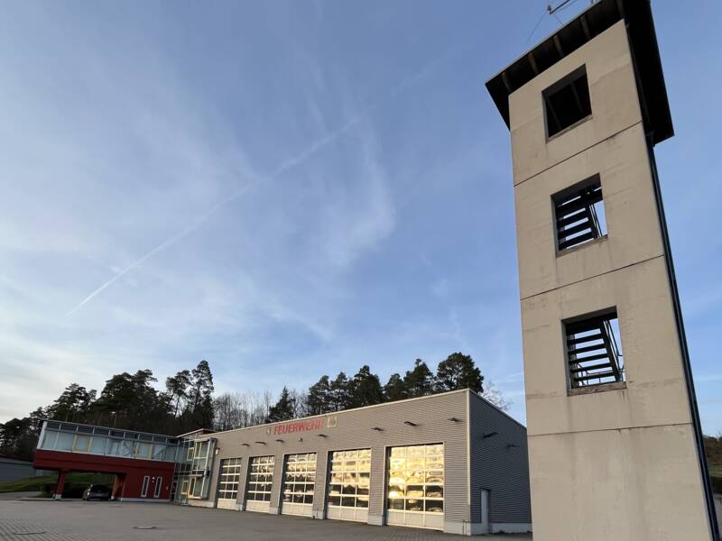 Glatt und grau ragt die Fassade des Schlauch- und Übungsturms der Feuerwehr auf.