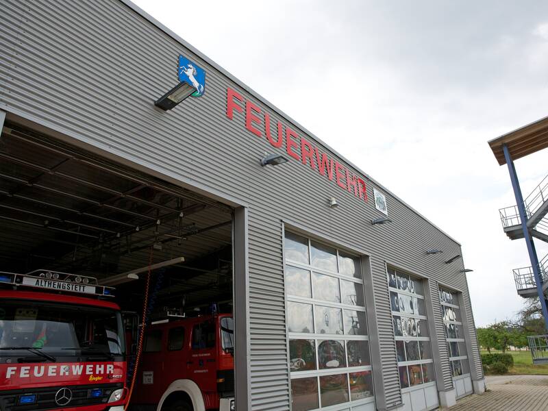 Durch das geöffnete Tor des Gerätehauses blitzen knallrot die Fahrzeuge der Feuerwehr.