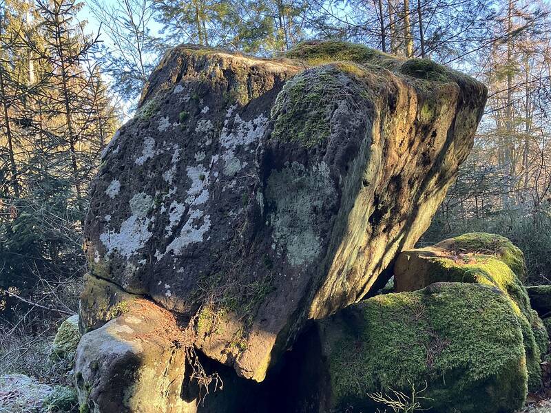 Ein Sandsteinblock ruht als großer Quader schief auf einer Steinplatte.