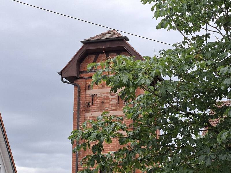 Blick aus dem Garten der Ortsverwaltung: Das alte Trafohäusle in Neuhengstett gleicht einem aus rotem Backstein erbauten Türmchen mit einem auf Fachwerk errichteten Dach.