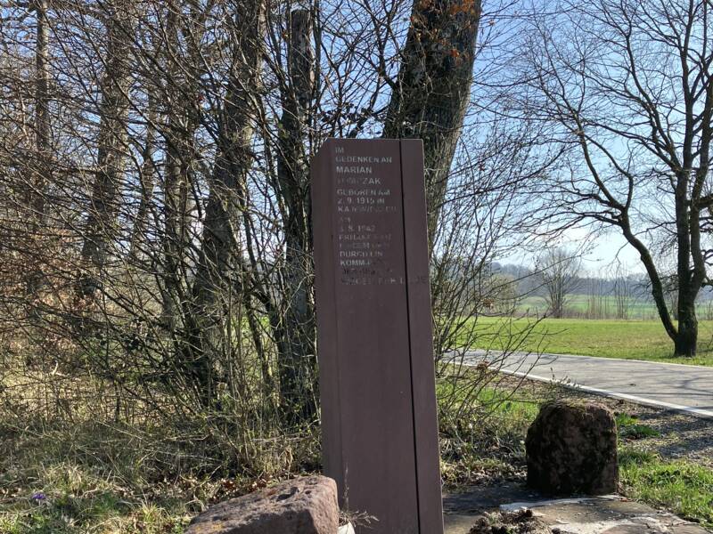Mehrere Buntsandsteinquader umstehen die Gedenstele Tomczak