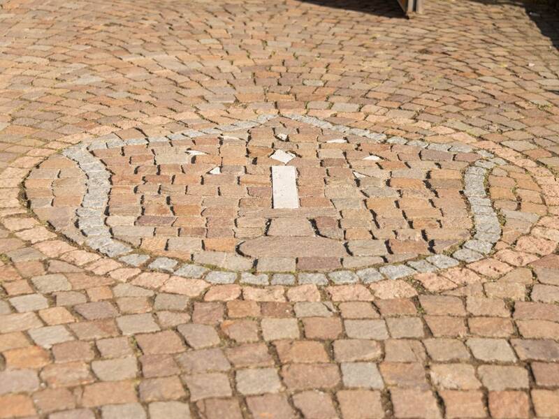 Auch vor der Kirche zeigt sich das aus Pflstersteinen gelegte Wappen der Waldenser: ein Leuchter, den sieben Sterne umgeben.