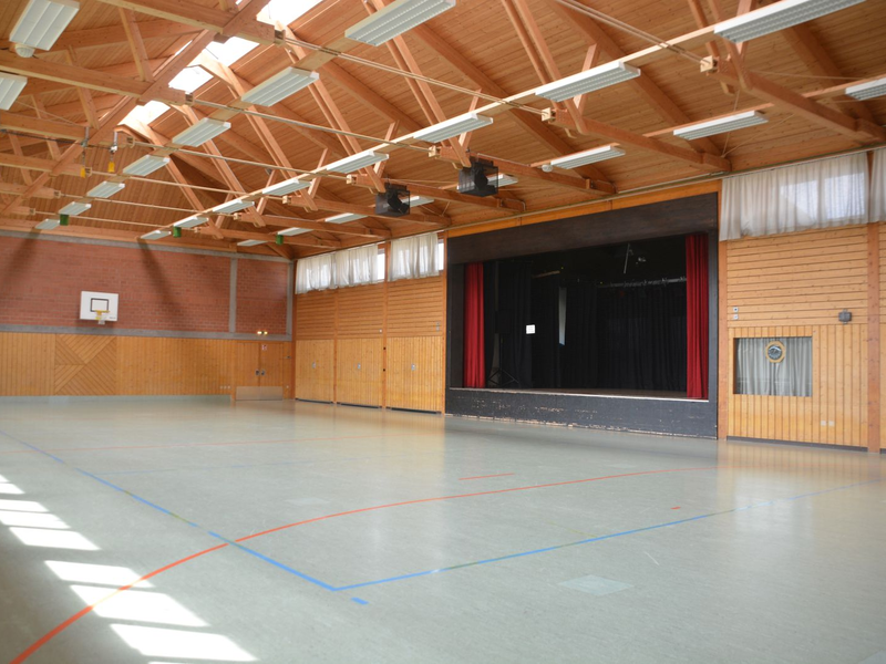 Durch die Fensterfront und die Fenster im Dach fällt viel Licht in die Mehrzweckhalle Ottenbronn. Rechts gähnt der schwarze Schlund der Bühne.