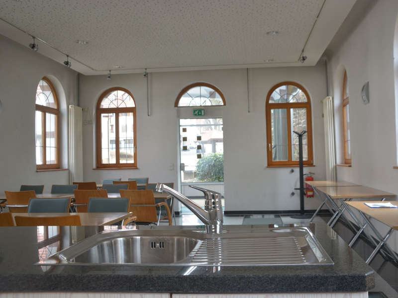 Blick über das Spülbecken der Teeküche in den Hauptraum mit Tischen und Stühlen.