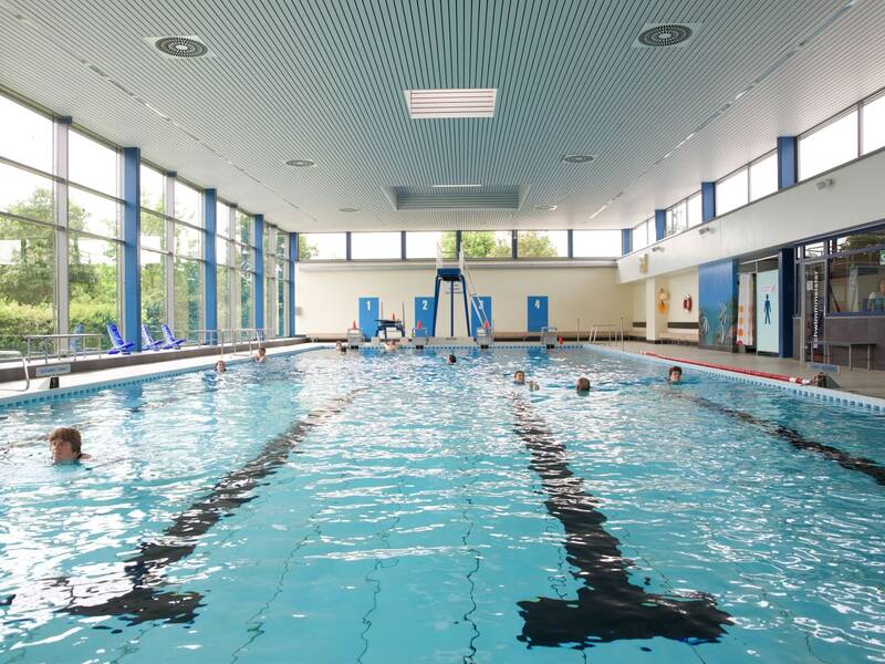 Bahnenschwimmen im lichtdurchfluteten Hallenbad, im Hintergund: der Spungturm mit Drei-Meter-Brett.
